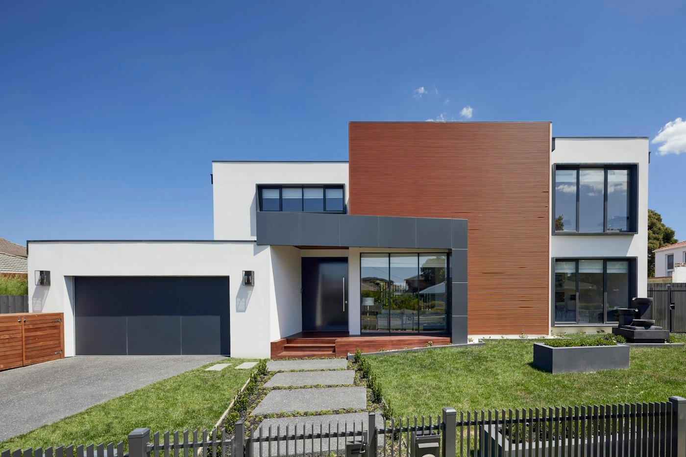 A white house with a timber panel, a dark garage door, and stepping stones across a lawn